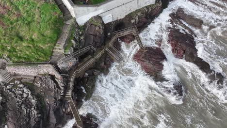 Drone-video-looking-straight-down-at-the-waves-crashing-against-the-walk-walk-and-rocks-beside-Youghal-Lighthouse-in-Youghal,-East-Cork,-Ireland