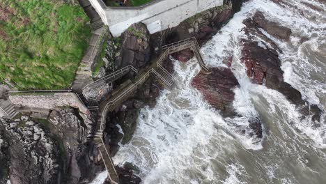 Drohnenvideo-Mit-Blick-Auf-Die-Wellen,-Die-Gegen-Den-Weg-Und-Die-Felsen-Neben-Dem-Leuchtturm-Von-Youghal-In-Youghal,-East-Cork,-Irland,-Schlagen