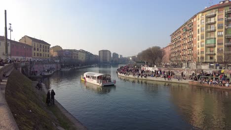 Tourists-pack-the-shores-as-a-tour-boat-rides-down-the-canal-in-Via-Vigevano,-Milan-Italy