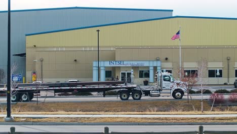 Aerial-establishing-shot-of-factory-warehouse-entrance-as-semi-truck-with-steel-beam-drives-past