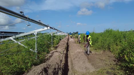 Trabajadores-Africanos-Con-Casco-Y-Ropa-De-Seguridad-Cavando-Zanjas-Para-La-Construcción-De-Una-Planta-De-Energía-Solar-En-Jambur,-Gambia