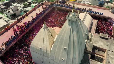 Vista-Aérea-Del-Dron:-El-Dron-Se-Mueve-Hacia-La-Cámara-Donde-Mucha-Gente-Juega-Dhuleti-Y-Que-Muestra-Un-Gran-Templo-Entre-Las-Casas.