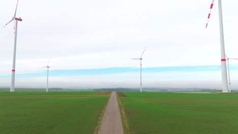 Eine-Straße-In-Grünen-Feldern-Mit-Hoch-Aufragenden-Windrädern