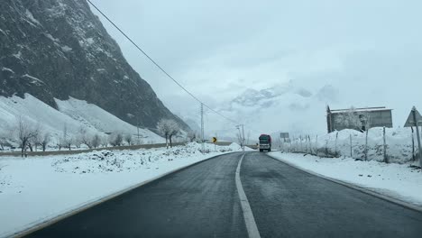 Car-driving-on-a-road-in-Skardu-in-landscape-covered-with-snow-and-high-mountains---It-is-cloudy-and-a-lorry-drives-past