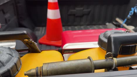 fire-safety-tools-sitting-in-the-back-of-a-black-lined-truck-bed-traffic-cone-indian-water-pump-cooler-ratchet-straps