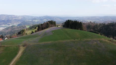 Erhöhte-Ansicht-Eines-Weitläufigen-Hügels-Mit-Wanderwegen,-Eingerahmt-Von-Violetten-Safran--Und-Krokusfeldern,-Einem-Flickenteppich-Aus-Wäldern-Und-Einer-Weiten,-Hügeligen-Landschaft,-Die-Sich-Bis-Zum-Horizont-Erstreckt,-Bei-Mrzli-Vrh