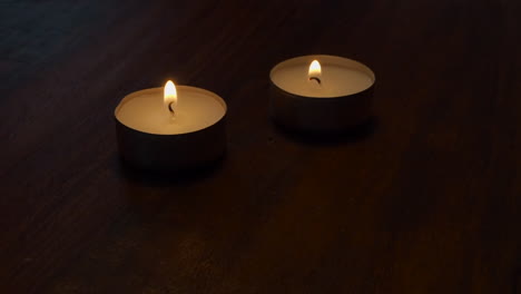 Room-lights-are-dimmed-as-two-tea-light-candles-burn-on-wood-table-top