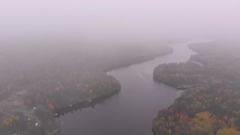 Aerial-pull-away-shot-revealing-a-Large-snaking-river-surrounded-by-stunning-fall-colored-trees-as-the-drone-eventually-flies-into-the-clouds