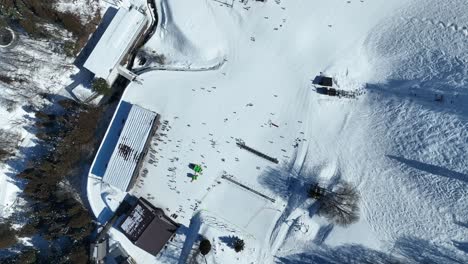 Draufsicht-Auf-Den-Unteren-Teil-Einer-Skipiste-In-Großer-Höhe,-Statische-Aufnahme-Von-Skifahrern,-Die-Am-Fuß-Des-Berges-Ankommen-Und-Sich-Für-Die-Sessellifte-Anstellen