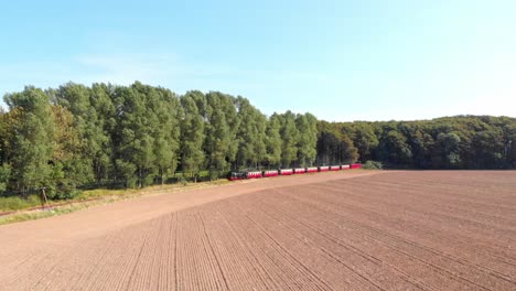 Aerial:-steam-narrow-gauge-railway-in-the-countryside-passing-by-sown-fields-and-some-trees