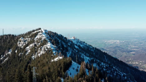 Cresta-De-Montaña-Cubierta-De-Nieve-Con-Vista-Aérea,-Cielo-Azul-Claro,-Con-Vistas-Al-Vasto-Bosque-Y-Al-Valle-Debajo