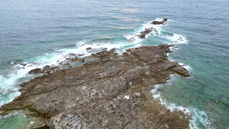 Linear-Tilt-Aerial-View-of-Rocky-Coastline-With-Green-Grass