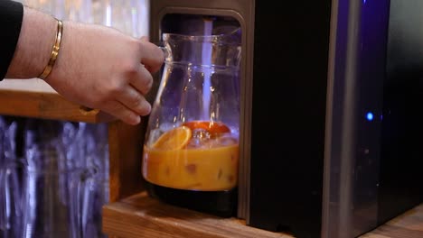 A-bartender-barista-preparing-a-lemonade-by-adding-soda-water-to-the-pitcher-with-fruit-and-syrup