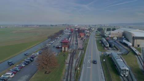 Una-Vista-Aérea-De-Una-Estación-De-Tren,-Con-Un-Tren-De-Pasajeros-A-Vapor-Acercándose-En-La-Distancia,-En-Un-Día-Parcialmente-Soleado.