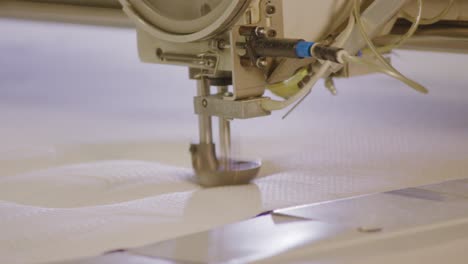 Industrial-sewing-machine-stitching-pattern-on-fabric,-close-up-in-boxspring-bed-factory