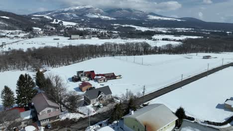 Empuje-Un-Disparo-De-Drone-Volando-Sobre-Casas-Y-Campos-Cubiertos-De-Nieve,-Con-Una-Zona-De-Esquí-Y-Un-Pueblo-De-Montaña-A-Lo-Lejos