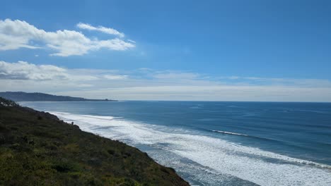 Malerische-Schwenkansicht-Des-Wanderweges-In-Torrey-Pines,-San-Diego-Mit-Blick-Auf-Die-Meereswellen,-Die-Gegen-Die-Küste-Krachen,-Und-Den-Blauen-Himmel