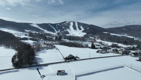 Drohne-Fotografiert-über-Schneebedeckten-Feldern,-Mit-Skigebiet-Und-Bergstadt-In-Der-Ferne