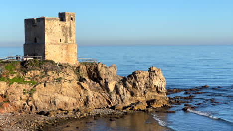 Torre-de-la-Sal-in-Casares-Manilva-beach-in-Spain,-coastal-tower-system-for-surveillance-and-defence-against-Berber-pirates,-green-plants-at-the-sunny-beach,-4K-static-shot