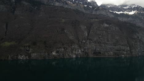 From-an-aerial-perspective,-witness-the-untamed-beauty-of-rugged-mountain-terrain-adorned-with-cascading-waterfalls,-framed-against-the-scenic-backdrop-of-Walensee-Unterterzen-in-Switzerland