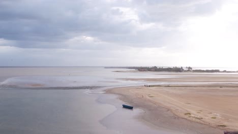 Aerial-drone-footage-captures-a-wet-sandy-beach-during-low-tide-in-Colombia,-with-a-stunning-sunset-in-the-background