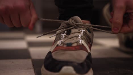 Close-up-of-hands-tying-the-laces-on-a-worn-sneaker,-indoor-lighting