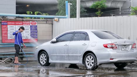 Carwasher-washing-and-spraying-soapy-water-on-a-sedan-in-a-carwash-shop-located-in-Bangkok,-Thailand