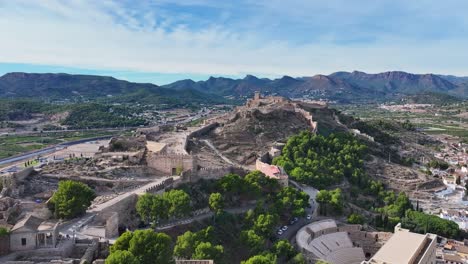 Rodaje-En-Alta-Calidad-Con-Un-Dron-Del-Castillo-De-Sagunto-Y-Sus-Murallas-Situadas-En-Una-Colina-Donde-También-Vemos-El-Anfiteatro-Romano-Con-Un-Fondo-De-Montañas-Y-Un-Cielo-Con-Nubes-Valencia-España