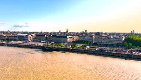 Approaching-Place-de-la-Bourse-plaza-square-in-Garonne-River-shore-with-large-dark-galleon-ship-in-Bordeaux-France,-Aerial-flyover-shot