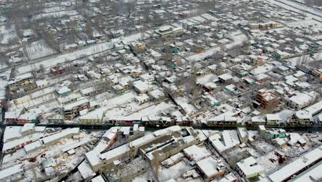 Drone-shot-of-the-city-of-Skardu-from-above,-snow-covered-and-a-road-with-cars