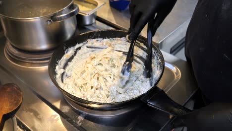 The-chef-stirs-pasta-in-creamy-mushroom-sauce-on-a-frying-pan