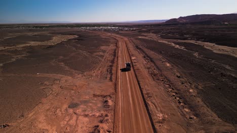 Truck-driving-on-dusty-road-through-Chilean-desert-landscape,-aerial-shot-in-bright-daylight