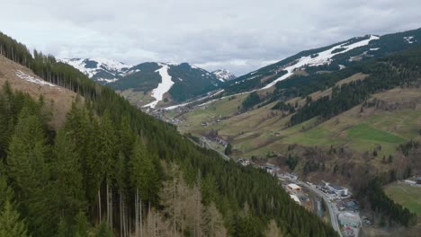 Exuberantes-Pinos-Verdes-Que-Enmarcan-Una-Pintoresca-Estación-De-Esquí-Austriaca-En-Saalbach-hinterglemm,-Rastros-De-Nieve-En-Las-Laderas,-Vista-Aérea