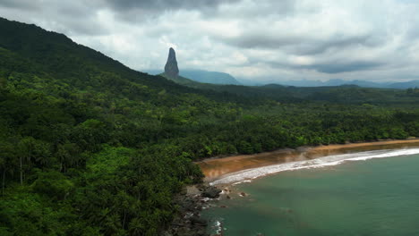 Aerial-view-in-front-of-the-Praia-Grande-beach-with-Pico-Cão-Grande-mountain-background,-in-cloudy-Sao-Tome