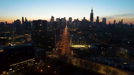 A-captivating-drone-aerial-view-panning-left-of-Chicago-at-dusk,-showcasing-illuminated-skyscrapers-against-the-darkening-sky-The-golden-hues-of-sunset-are-highlighting-architectural-marvels