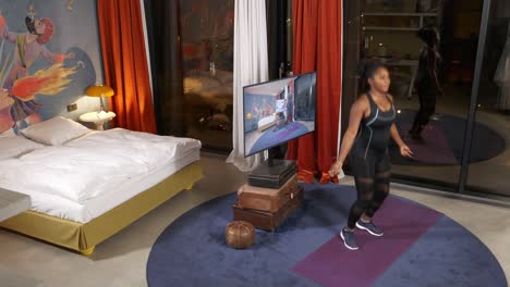 Woman-in-athletic-wear-prepares-to-exercise-in-a-modern-bedroom,-doing-jumps,-TV-and-decor-visible,-evening