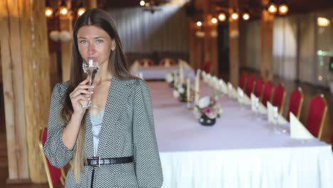 Young-attractive-woman-posing-and-drinking-champagne-in-front-of-a-big-event-dinner-table-at-a-restaurant