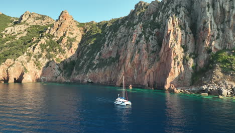 Sailboat-cruising-in-the-serene-blue-waters-of-Golf-de-Girolata,-Corsica,-flanked-by-rugged-cliffs