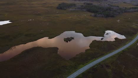 Aerial-landscape-above-skyline-reflected-at-countryside-lake-in-Isle-of-Skye,-Scotland-road-through-fields