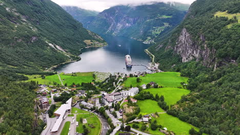 Aerial-View-of-Scenic-Geiranger-Fjord-and-Cruise-Ship-Anchored-by-Village-and-Green-Hills,-Norway