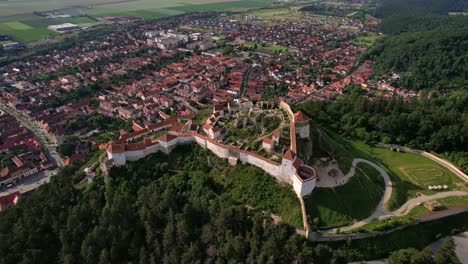 Ciudadela-De-Rasnov-En-Rumania-Con-Ciudad-Y-Paisaje-Verde-A-La-Luz-Del-Día,-Vista-Aérea