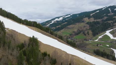 Melting-snow-on-slopes-of-Saalbach-Hinterglemm-,-patchy-green,-aerial-shot