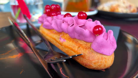 Delicious-eclair-with-forest-berry-cream-on-a-plate-at-a-bakery,-choux-dough-pastry-filled-with-purple-cream,-sweet-dessert,-4K-shot