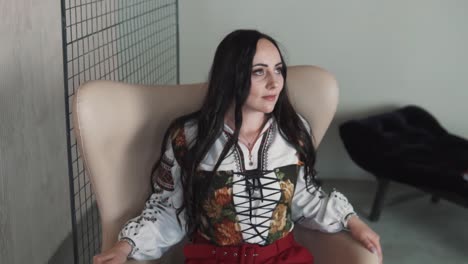 lovely-young-woman-sits-in-a-chair-dressed-in-a-fashionable-embroidered-authentic-Ukrainian-shirt-and-corset