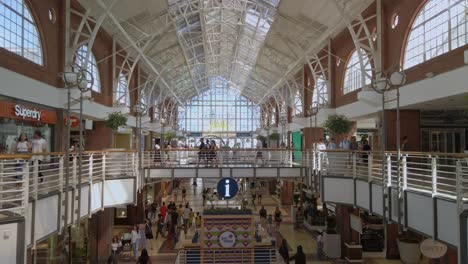 Panoramic-wide-static-shot-inside-shopping-mall-at-south-Africa-cape-town-modern-architecture-of-wooden-white-stores-and-people-buying-inside-commercial-area