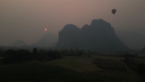 "Aerial-view-at-sunset-over-a-mountain-with-a-hot-air-balloon-amidst-the-stunning-backdrop-of-the-sun's-glow-amid-forest-fire-smoke