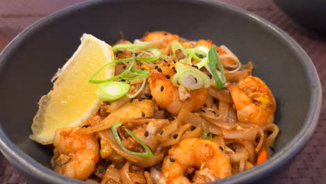 Traditional-Pad-Thai-wok-noodles-with-shrimps,-spring-onion-and-a-lemon-slice,-Thai-restaurant,-tasty-Asian-food,-4K-shot