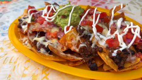 Traditional-Tex-Mex-Mexican-nachos-with-beef-chilli-con-carne,-guacamole,-melted-cheese-and-sour-cream,-totopos-tortilla-chips,-tasty-food,-4K-shot