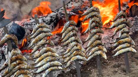 Traditional-Spanish-sardines-Espetos-fish-grilled-at-the-beach-over-fire-on-metal-skewers-in-Marbella-Malaga-Spain,-delicious-seafood,-4K-shot