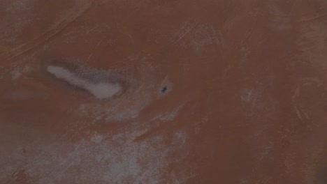 Overhead-drone-clip-of-dry-and-cracked-desert-floor,-with-man-lying-on-ground-in-wetsuit-to-highlight-drought-and-water-shortages-due-to-climate-change